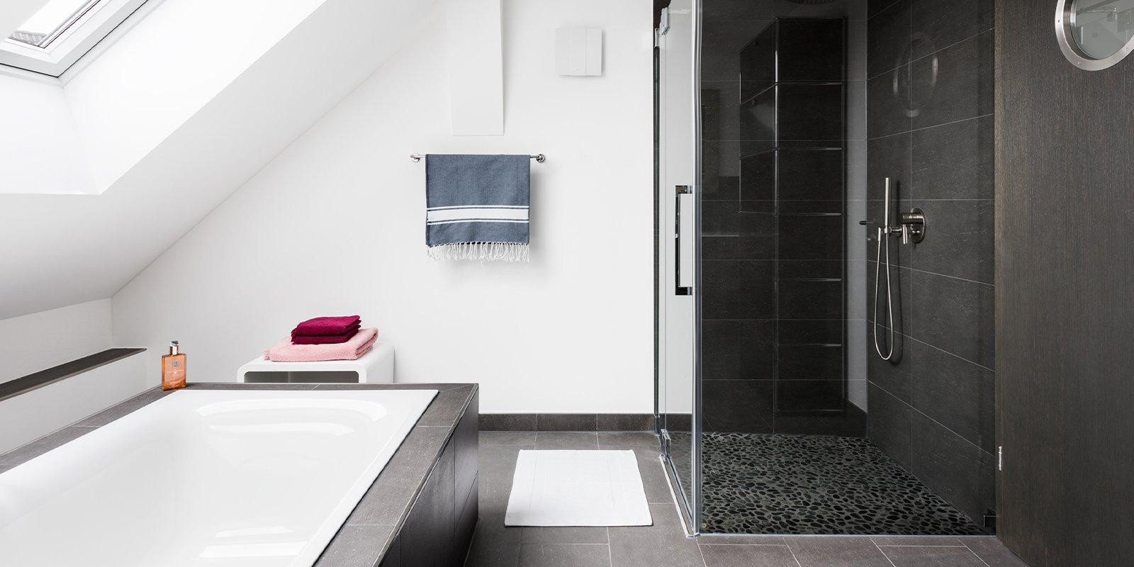 Ein modernes Badezimmer mit einer freistehenden Badewanne und einer eleganten Dusche, die mit dunklen Fliesen gestaltet ist.