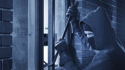 Ein Einbrecher der ein Fenster mit einer Brechstange öffnet