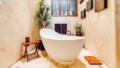 Ein elegantes Badezimmer mit einer freistehenden Badewanne, umgeben von Pflanzen und sanften Erdtönen an den Wänden.