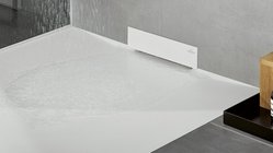 Ein moderner Duschbereich mit einem weißen Boden, auf dem Wasser steht, und einer eleganten Wandverkleidung aus Beton.